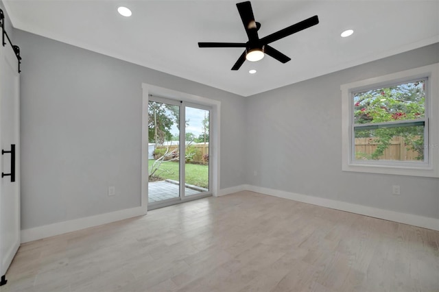 unfurnished room with ceiling fan, a barn door, and light hardwood / wood-style floors