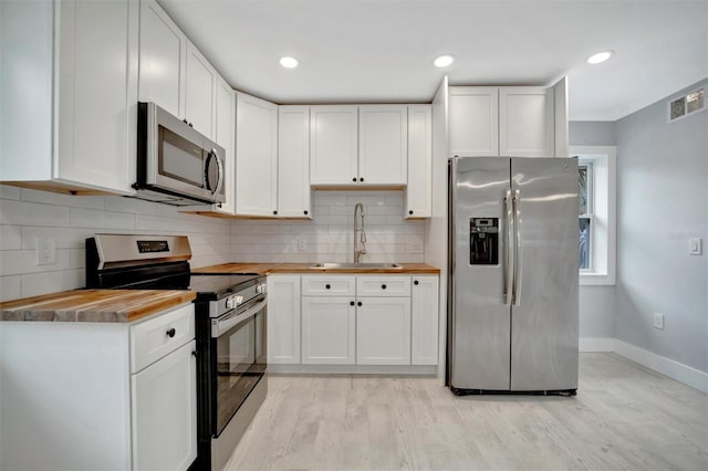 kitchen featuring appliances with stainless steel finishes, tasteful backsplash, white cabinetry, butcher block counters, and sink