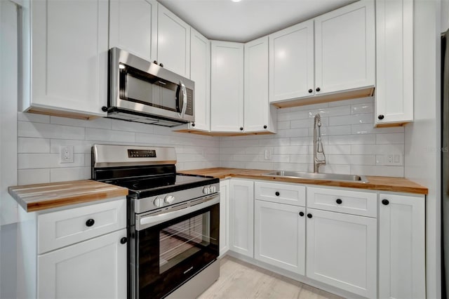 kitchen with stainless steel appliances, butcher block counters, sink, and white cabinets