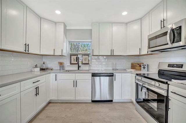 kitchen with stainless steel appliances, a sink, light countertops, white cabinets, and recessed lighting