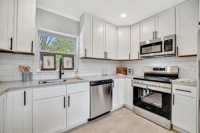 kitchen featuring appliances with stainless steel finishes, a sink, light countertops, white cabinetry, and recessed lighting