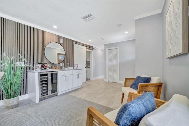 living room with wine cooler, bar area, a barn door, baseboards, and light wood-style flooring
