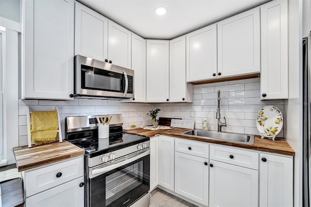 kitchen featuring wooden counters, stainless steel appliances, a sink, and white cabinetry