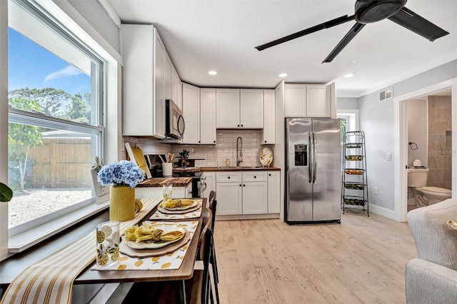 kitchen with appliances with stainless steel finishes, light wood finished floors, a ceiling fan, tasteful backsplash, and baseboards