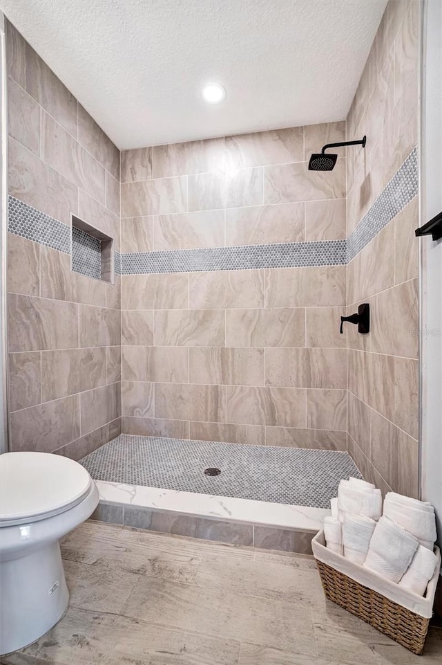 bathroom featuring a textured ceiling, tiled shower, and toilet