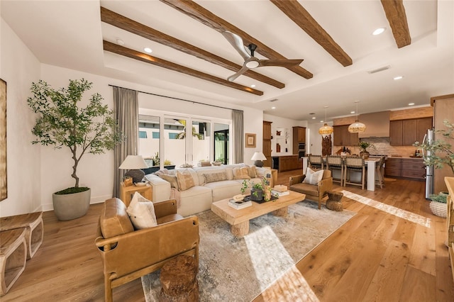 living area with ceiling fan, beamed ceiling, light wood-type flooring, and visible vents