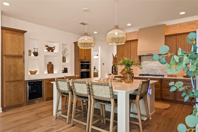 kitchen featuring wine cooler, premium range hood, light countertops, a kitchen bar, and decorative light fixtures