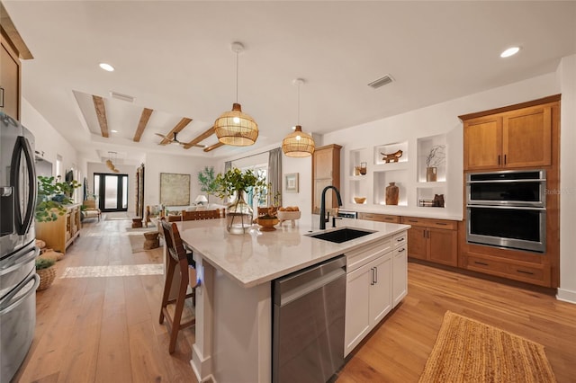 kitchen with hanging light fixtures, appliances with stainless steel finishes, white cabinets, a sink, and an island with sink