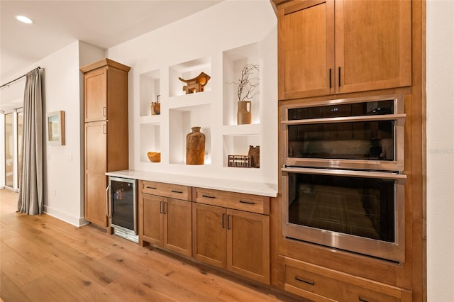 kitchen featuring brown cabinets, light countertops, double oven, light wood-style floors, and beverage cooler