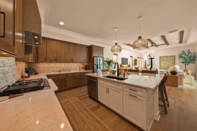 kitchen with a kitchen island with sink, a sink, open floor plan, appliances with stainless steel finishes, and pendant lighting