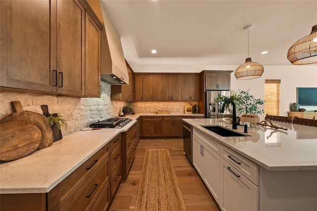 kitchen featuring stainless steel appliances, an island with sink, a sink, and pendant lighting