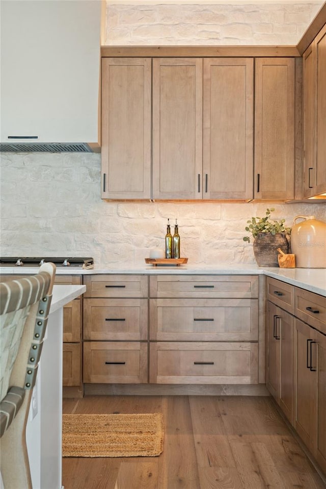 kitchen with tasteful backsplash, range hood, light countertops, and light wood-style flooring