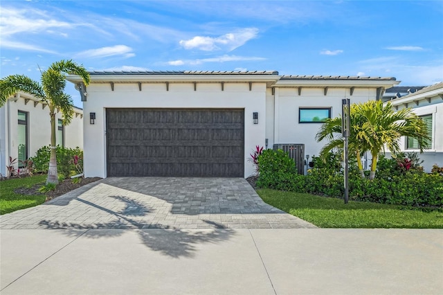 view of front facade featuring decorative driveway, a tiled roof, an attached garage, and stucco siding