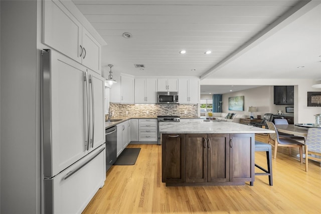 kitchen with a breakfast bar area, appliances with stainless steel finishes, a center island, light stone countertops, and white cabinets