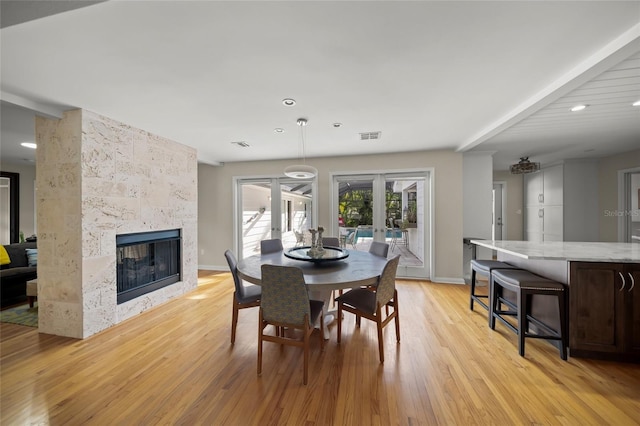 dining room featuring a tiled fireplace, light hardwood / wood-style floors, and french doors