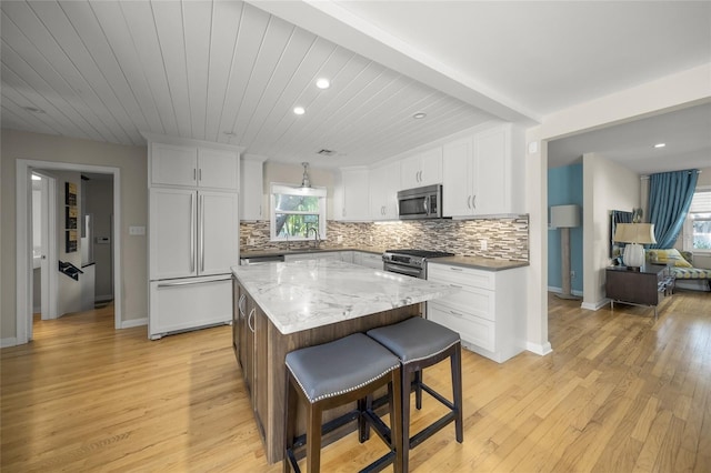 kitchen featuring stainless steel appliances, white cabinetry, a kitchen island, and tasteful backsplash