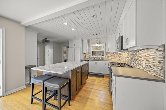 kitchen with sink, white cabinetry, a kitchen island, stainless steel appliances, and backsplash