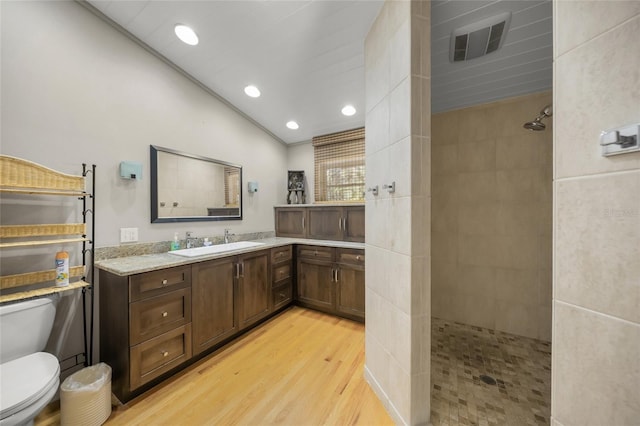 bathroom featuring lofted ceiling, hardwood / wood-style flooring, tiled shower, vanity, and toilet