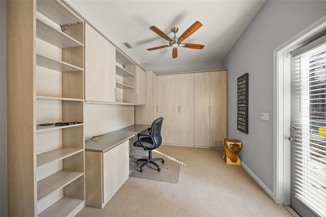 unfurnished office with built in desk, light colored carpet, and ceiling fan