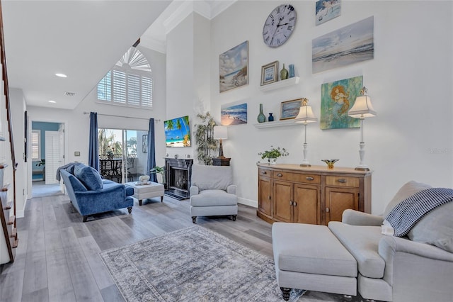 living room featuring crown molding, light hardwood / wood-style flooring, and a high ceiling