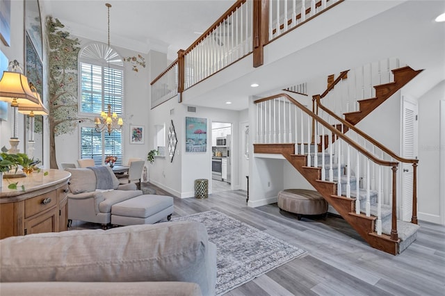 living room featuring crown molding, a chandelier, a high ceiling, and light wood-type flooring