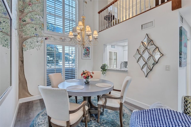 dining area with an inviting chandelier, sink, wood-type flooring, and a high ceiling