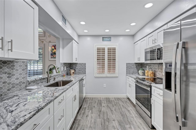 kitchen with sink, stainless steel appliances, light stone counters, light hardwood / wood-style floors, and white cabinets