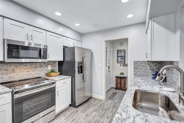 kitchen with white cabinetry, sink, light stone counters, stainless steel appliances, and light wood-type flooring