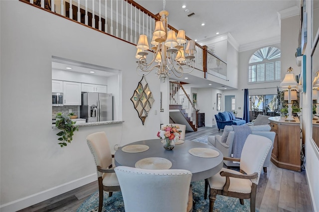 dining room with hardwood / wood-style floors, a towering ceiling, ornamental molding, and a chandelier