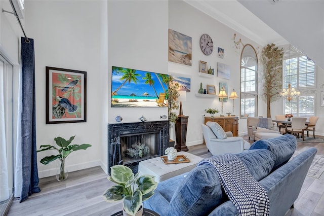 living room featuring a towering ceiling, an inviting chandelier, a fireplace, and light hardwood / wood-style flooring