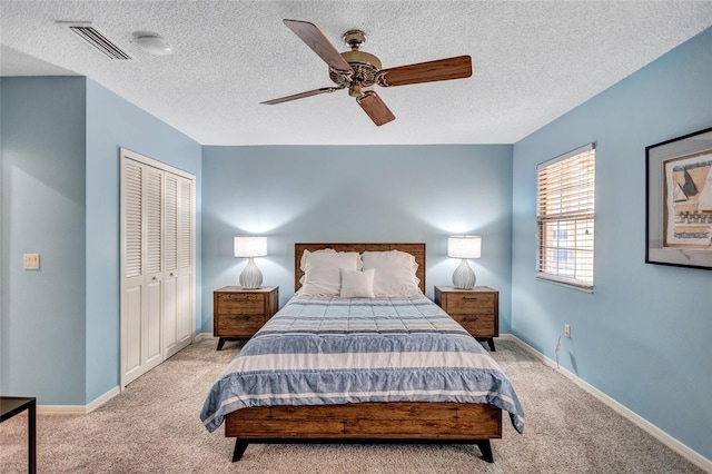 bedroom featuring ceiling fan, light colored carpet, a closet, and a textured ceiling