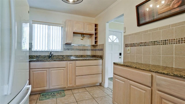 kitchen with light brown cabinetry, sink, dark stone counters, and white fridge