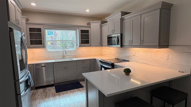 kitchen featuring appliances with stainless steel finishes, sink, a kitchen bar, kitchen peninsula, and light hardwood / wood-style flooring