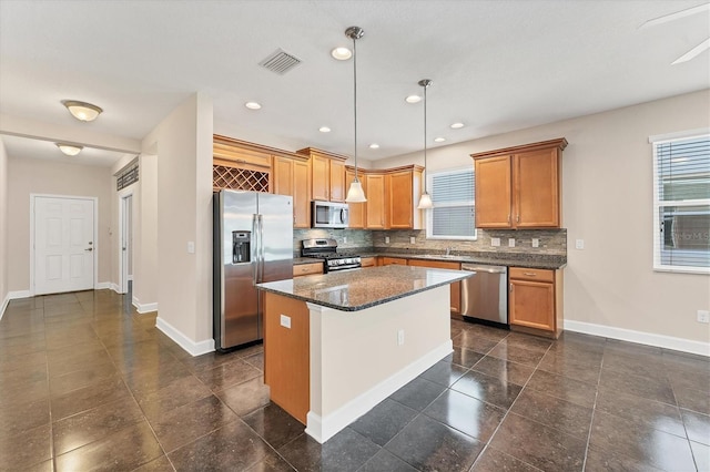 kitchen featuring dark stone countertops, appliances with stainless steel finishes, a kitchen island, pendant lighting, and decorative backsplash