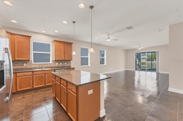 kitchen with hanging light fixtures, a kitchen island, backsplash, and dark stone counters