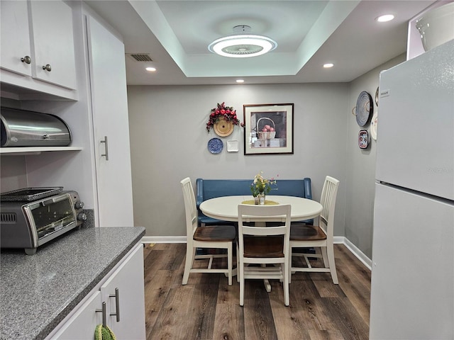 dining room with a toaster, dark wood finished floors, baseboards, visible vents, and a raised ceiling