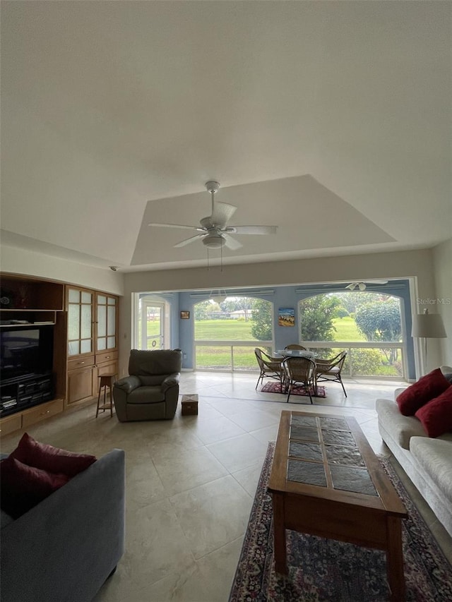 tiled living room with ceiling fan and a tray ceiling