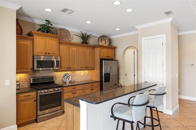 kitchen featuring dark stone countertops, light tile patterned flooring, stainless steel appliances, and a center island with sink