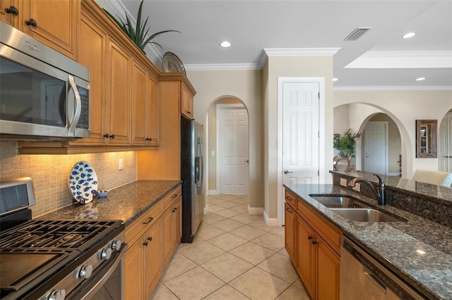 kitchen featuring sink, crown molding, dark stone counters, stainless steel appliances, and backsplash