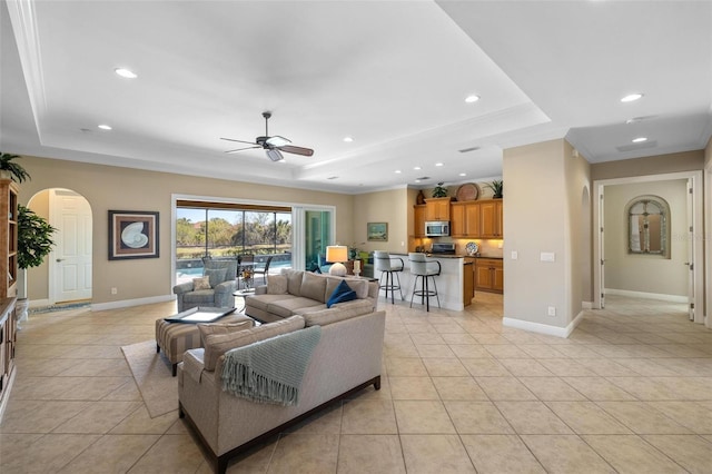 living room with light tile patterned floors, ceiling fan, and a tray ceiling