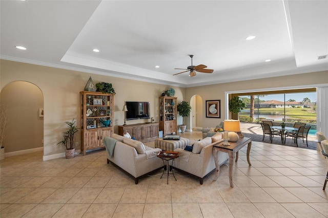 tiled living room with ornamental molding, ceiling fan, and a tray ceiling