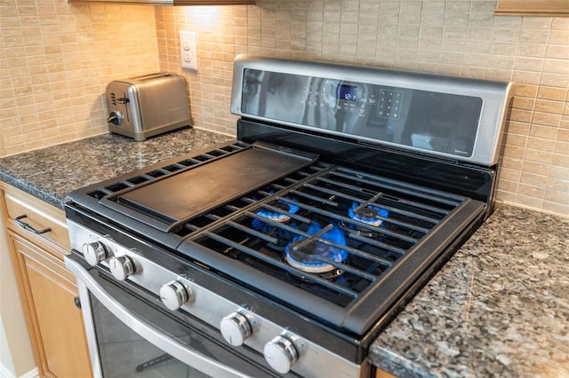 details featuring stainless steel gas stove, backsplash, and dark stone countertops