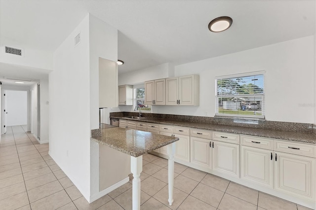 kitchen featuring light tile patterned flooring, a breakfast bar, sink, dark stone countertops, and kitchen peninsula