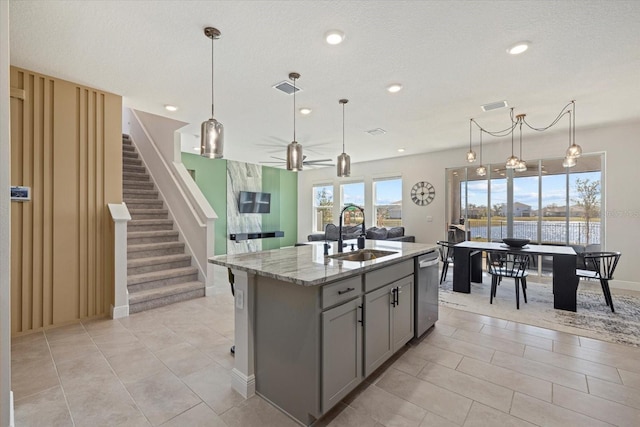 kitchen with sink, a kitchen island with sink, gray cabinetry, light stone counters, and decorative light fixtures