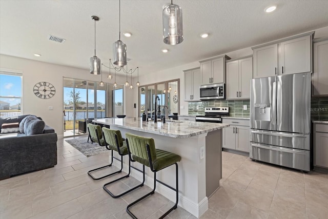 kitchen with stainless steel appliances, pendant lighting, a kitchen island with sink, and gray cabinetry