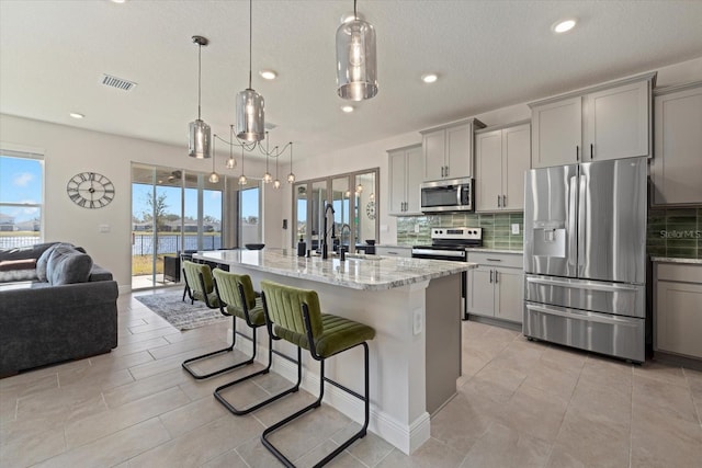 kitchen with a kitchen island with sink, hanging light fixtures, gray cabinets, and appliances with stainless steel finishes