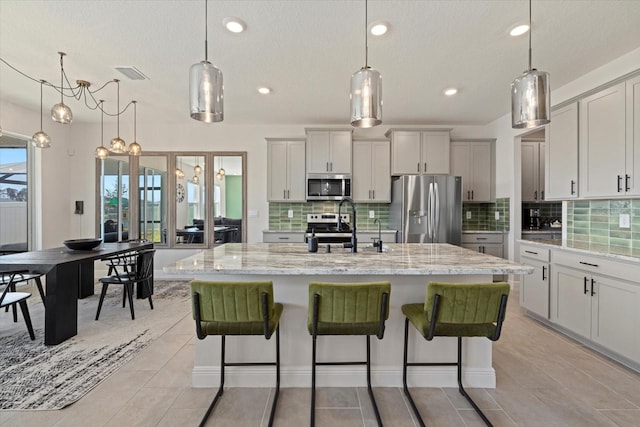 kitchen featuring stainless steel appliances, an island with sink, and decorative light fixtures