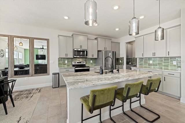 kitchen featuring a kitchen island with sink, hanging light fixtures, stainless steel appliances, a kitchen breakfast bar, and light stone counters