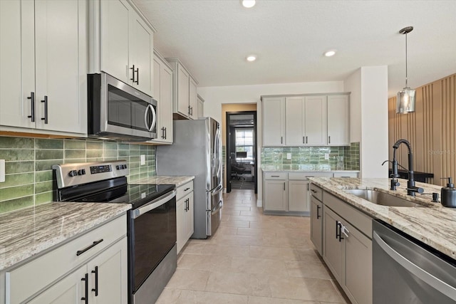 kitchen with sink, hanging light fixtures, appliances with stainless steel finishes, light stone countertops, and backsplash