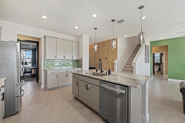 kitchen featuring an island with sink, stainless steel appliances, gray cabinets, and sink